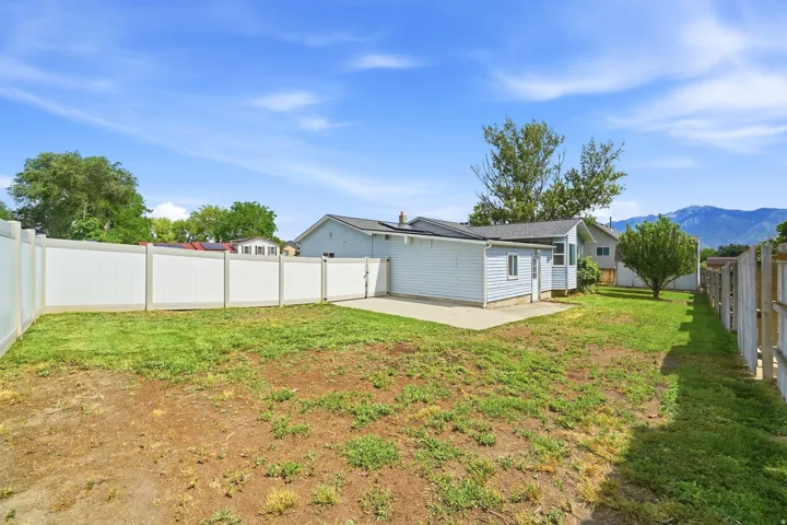 Expansive backyard featuring a white privacy fence, mature trees, and a concrete patio