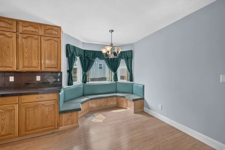 Built-in corner banquette seating with a bay window, wood-finish flooring, and recessed panel cabinetry with a dark countertop