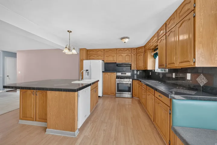 Kitchen featuring wood-finish flooring, wood cabinetry, a center island with a sink, stainless steel range, and tile countertops