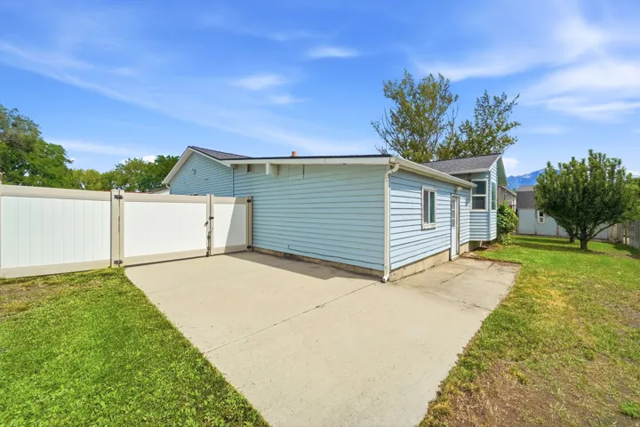 Expansive concrete patio with a privacy fence and gate, surrounded by a grassy area and mature trees
