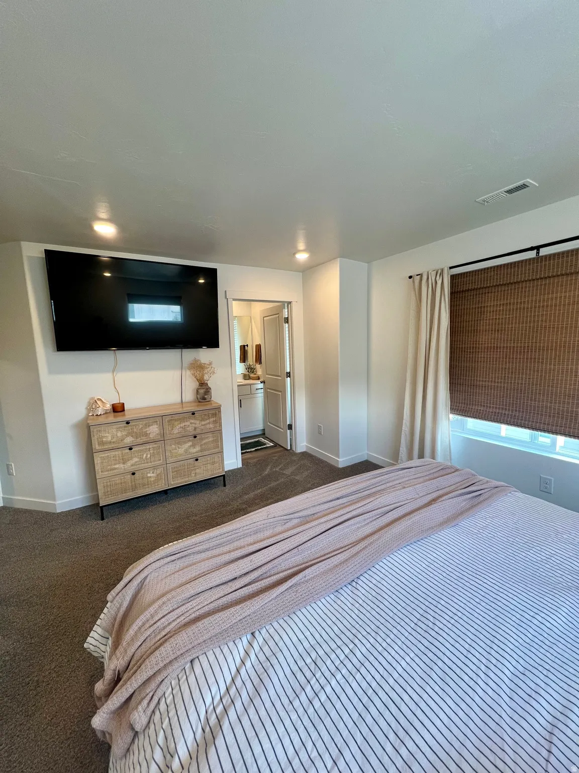 Recessed ceiling lighting, wall-mounted television, and a window with a woven shade and drapes