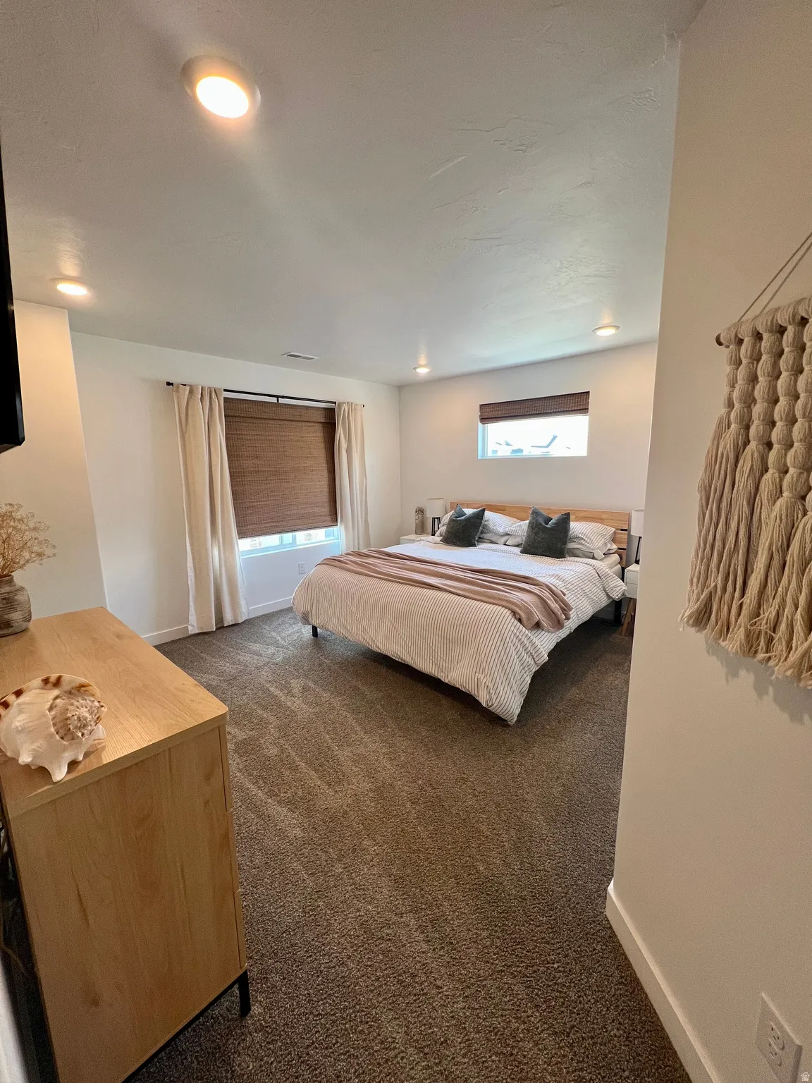Recessed lighting illuminates the space, featuring plush carpeting and a window with blinds