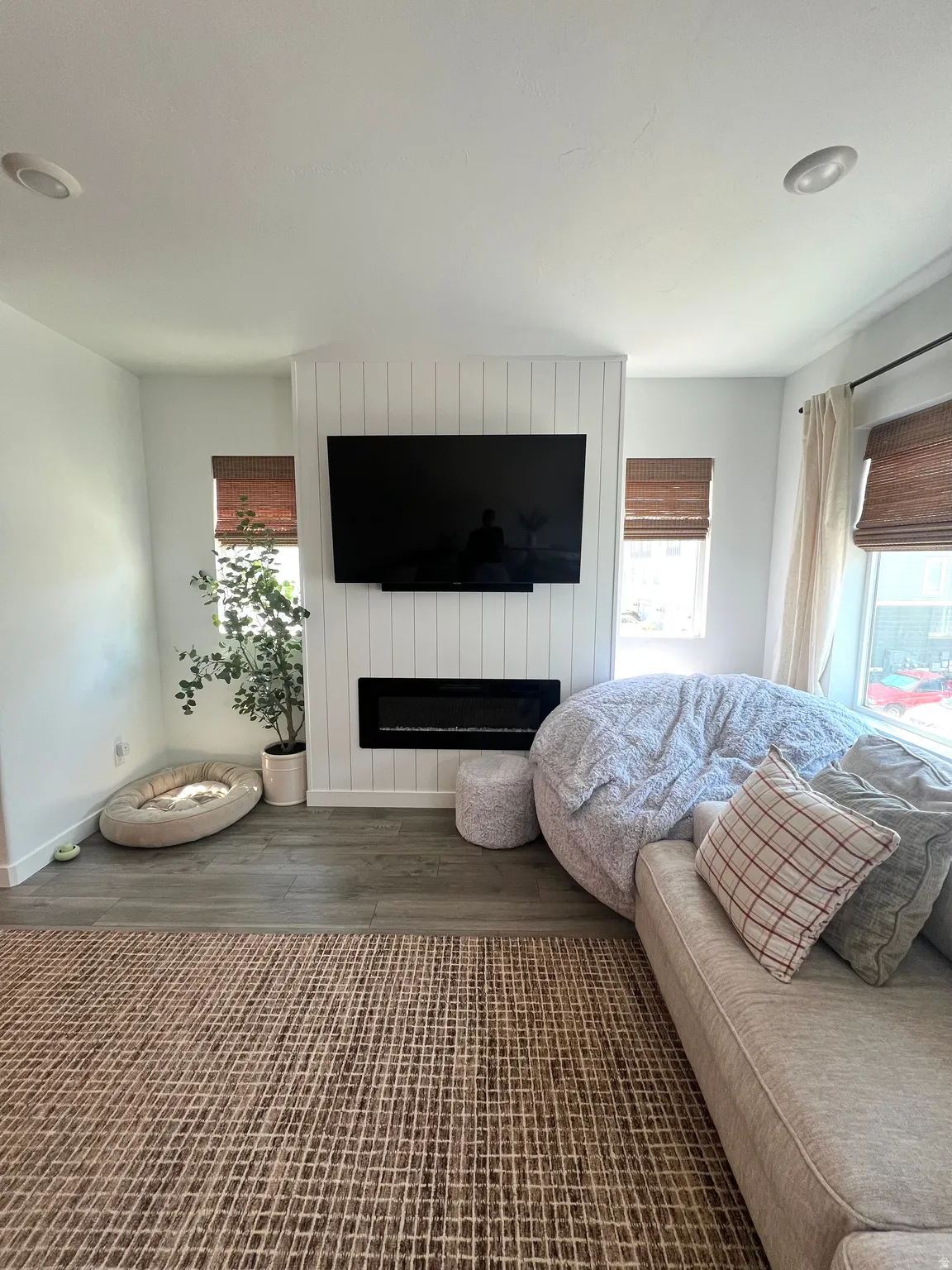 Recessed lighting, wood-finish flooring, white shiplap accent wall, built-in linear fireplace, and window treatments