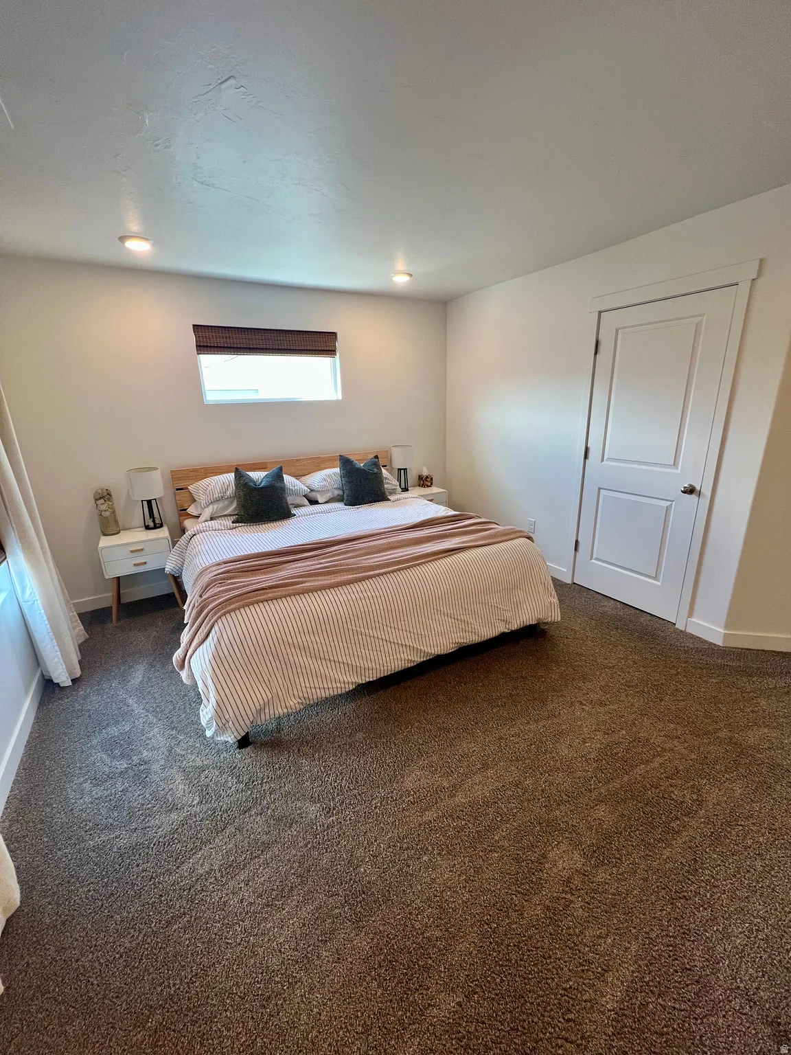 Recessed ceiling lighting, a window with a wood-finish blind, plush carpet, and a paneled interior door