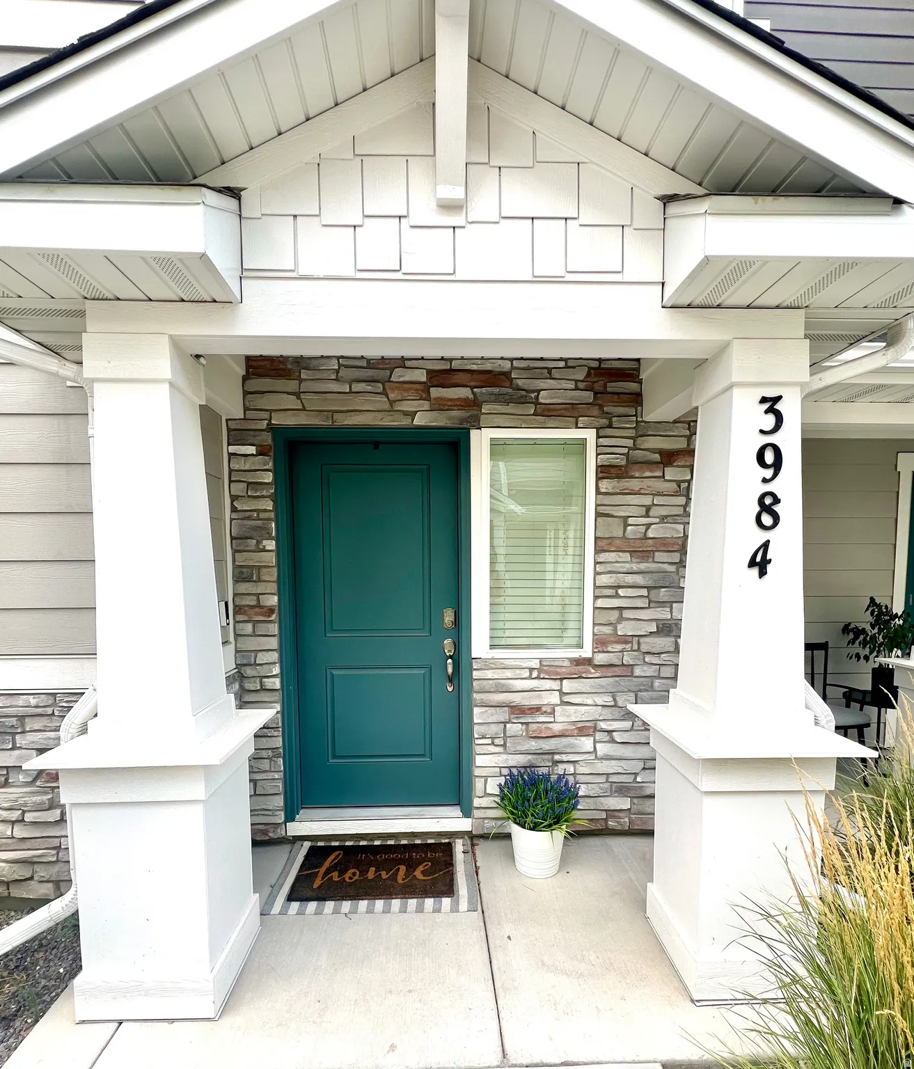Covered entry featuring a teal door, stacked stone accent wall, and vinyl shake siding