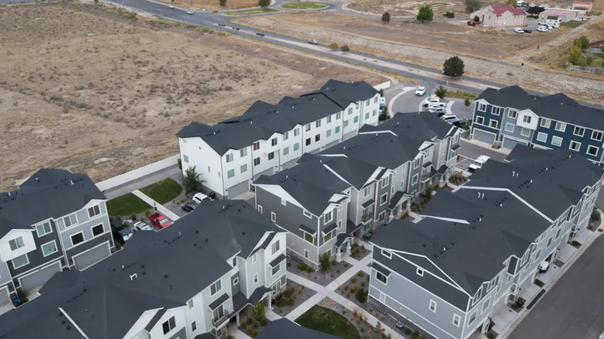 Community of multi-story residences with attached garages, individual driveways, and dark gray roofs