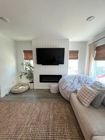 Recessed lighting, wood-finish flooring, white shiplap accent wall, built-in linear fireplace, and window treatments