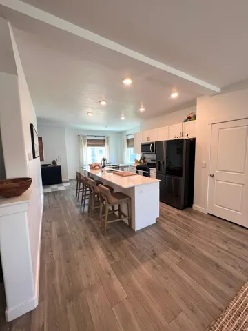 Wood-finish flooring throughout, kitchen island with seating, recessed lighting, white cabinetry, and stainless steel appliances