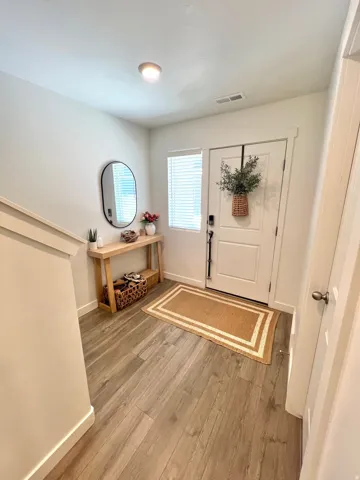 Wood-finish flooring, white entry door with frosted glass panel, recessed ceiling light, and a window with blinds