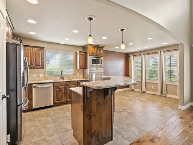 Kitchen featuring wood cabinetry, stainless steel appliances, a center island with a stone countertop, and recessed lighting