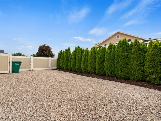 Gravel lot featuring a privacy fence, dense evergreen hedge, and a neutral-toned building exterior