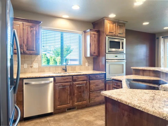 Wood cabinetry with stone countertops, stainless steel built-in appliances, recessed lighting, and tile flooring