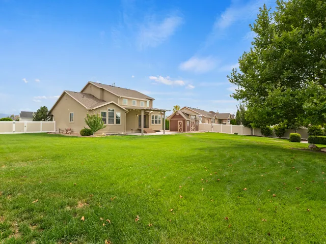 Expansive green lawn, stucco exterior, rear patio with pergola, detached shed structure, and white privacy fencing