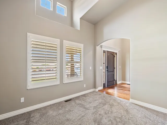 Vaulted ceiling with upper windows, plantation shutters, arched doorway, and wood-finish flooring