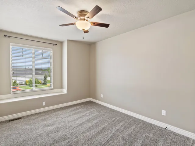 Spacious room with plush gray carpeting, a window bench, and a ceiling fan with integrated lighting