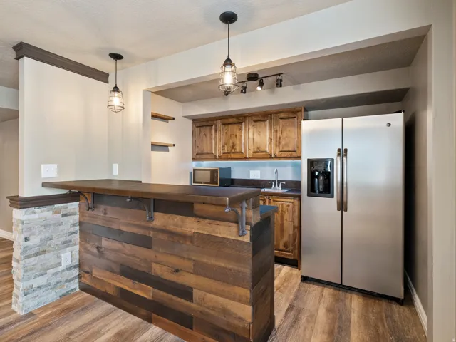 Built-in bar with wood-finish flooring, stone accent wall, and recessed lighting