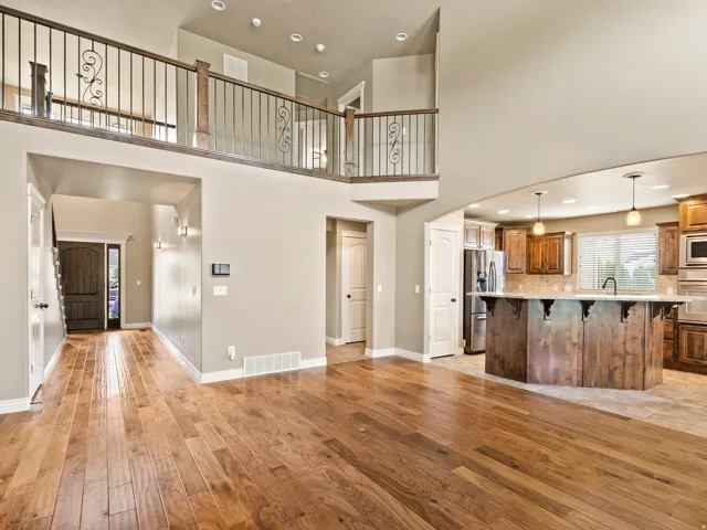 Open-concept living area with wood-finish flooring, a two-story ceiling, and an open balcony with wrought iron railing