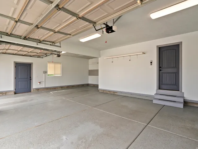 Spacious garage with two overhead doors, epoxy flooring, two panel doors, and overhead lighting