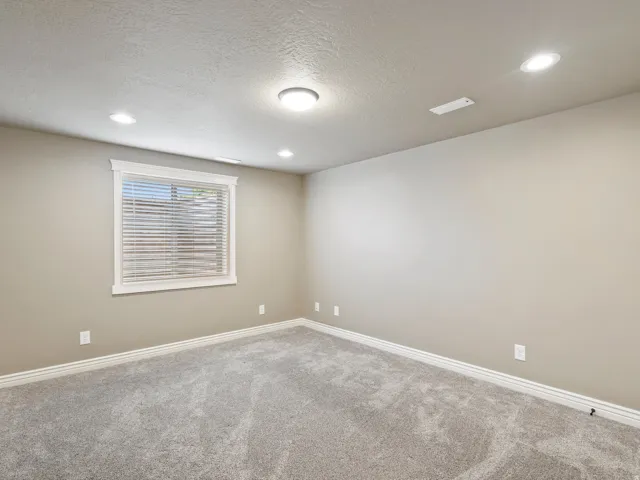 Recessed lighting, neutral wall paint, white trim, window with blinds, and textured carpeting