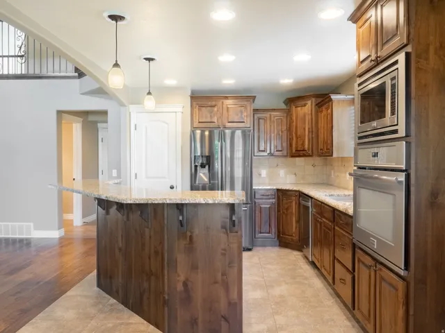 Kitchen featuring wood cabinetry, stainless steel appliances, a tiled backsplash, a kitchen island with stone countertops, and recessed lighting