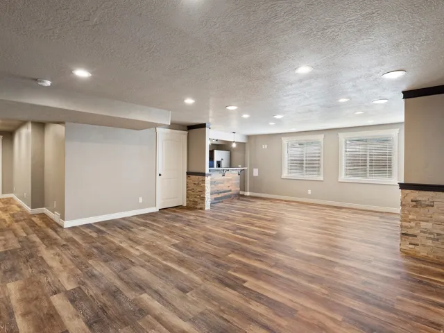 Spacious lower-level area featuring wood-finish flooring, recessed lighting, and a built-in bar with stone-look detailing