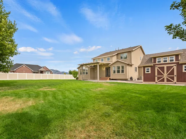 Expansive green lawn with a pergola-covered patio, a stucco exterior, and a detached barn structure