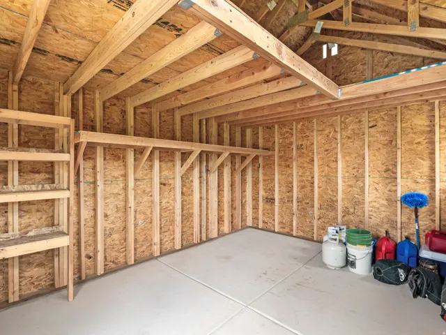 Unfinished interior space featuring exposed wood framing, oriented strand board walls, a high vaulted ceiling, built-in shelving, and a concrete floor