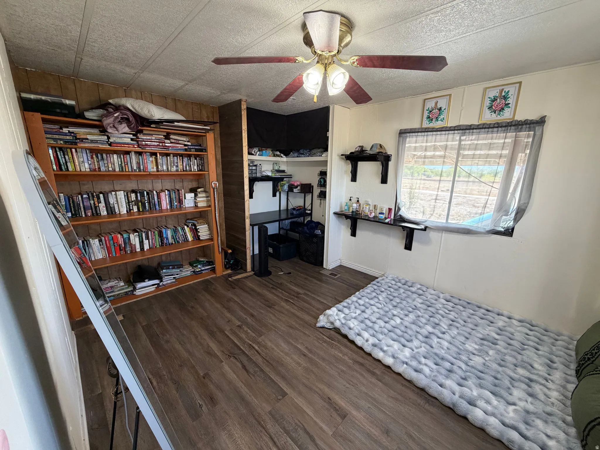 Wood-finish flooring, built-in shelving, ceiling fan with integrated lighting, and a window for natural light