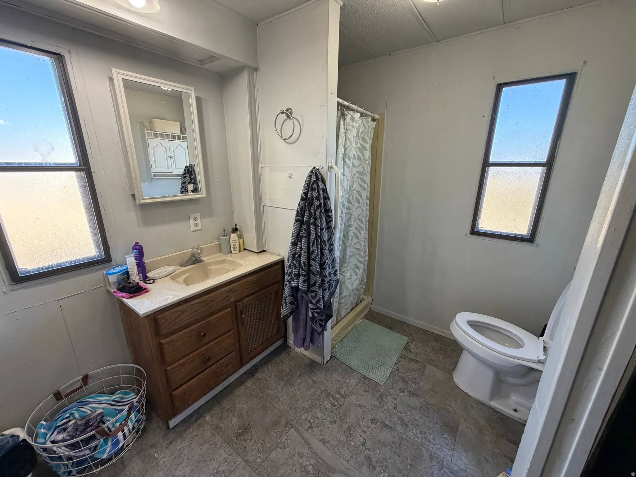 Bathroom featuring a single vanity with wood cabinetry, a built-in shower stall, a toilet, and two windows