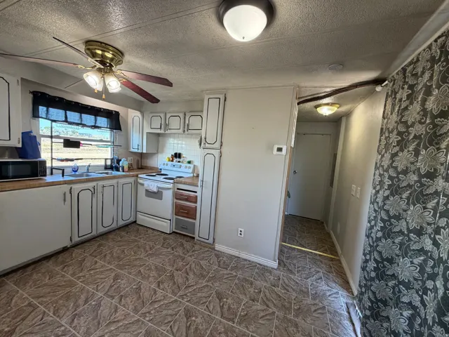 Kitchen featuring laminate countertops, white cabinetry, a built-in oven, and a ceiling fan with integrated lighting