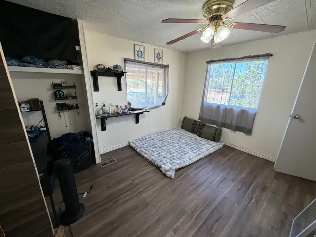 Wood-finish flooring, white paneled walls, two windows, and a ceiling fan with integrated lighting