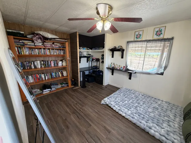 Wood-finish flooring, built-in shelving, ceiling fan with integrated lighting, and a window for natural light