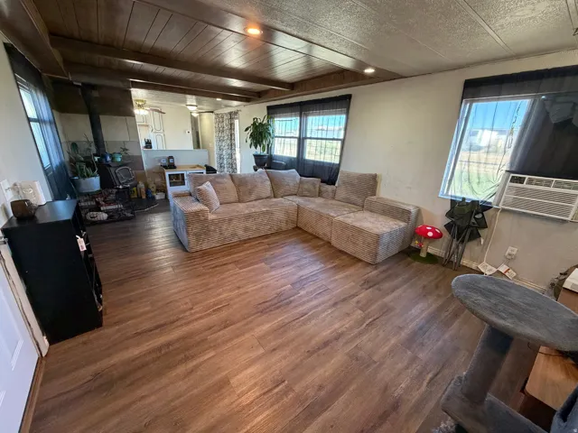 Wood-finish flooring, wood-paneled ceiling, multiple windows, built-in wood-burning stove, and a partial kitchen visible