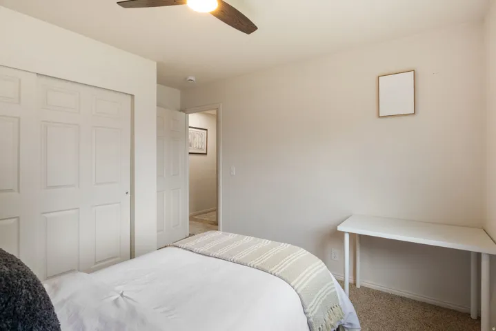 Integrated ceiling fan with light fixture, neutral wall color, white bi-fold closet doors, and light-toned carpeting
