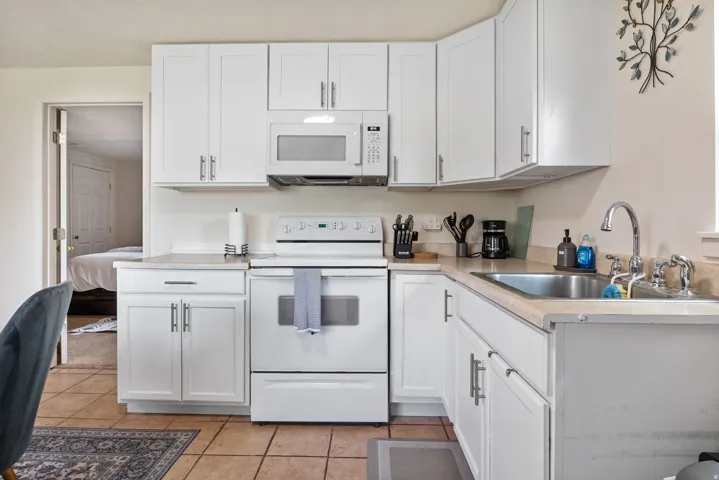 Kitchen featuring white cabinetry, light-toned countertops, a stainless steel sink, and tile flooring