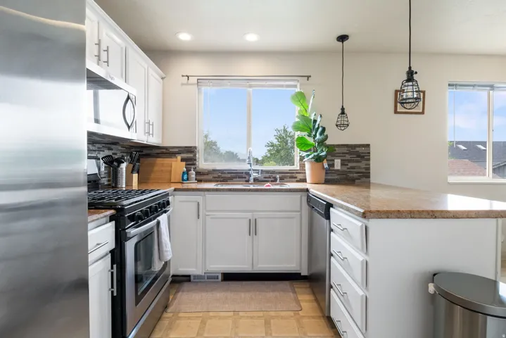 Kitchen featuring white cabinetry, stainless steel appliances, a tiled backsplash, a built-in dishwasher, and pendant lighting