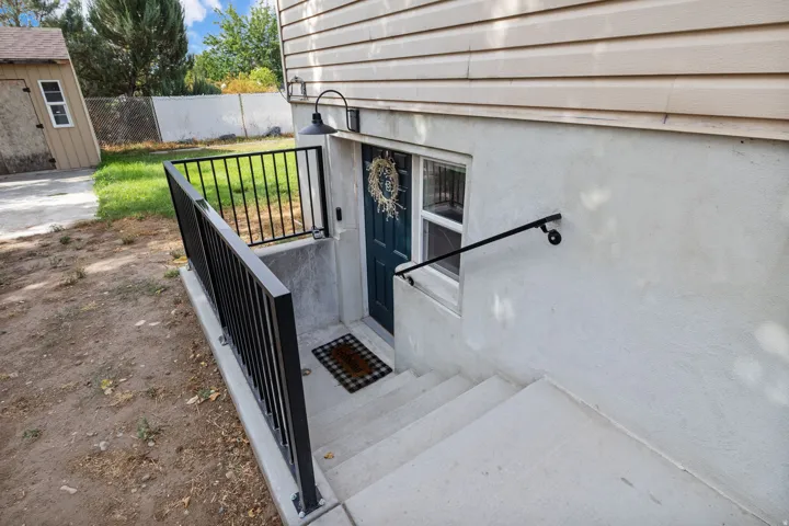 Concrete steps with black metal railings, a dark-colored entry door, and a window well, all under tan siding