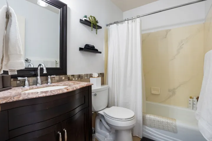 Dark wood-finish vanity with a built-in basin and polished chrome faucet, mosaic tile backsplash, framed wall mirror, and a built-in tub with a shower enclosure