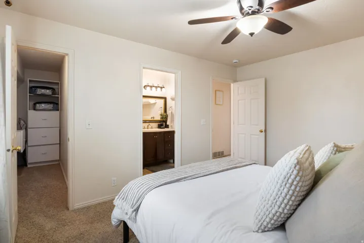 Bedroom with a ceiling fan, carpeted flooring, and a built-in closet organization system