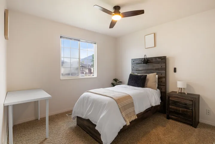 Neutral wall color, window with exterior scenery, overhead ceiling fan, carpeted flooring, wood-finish bed frame