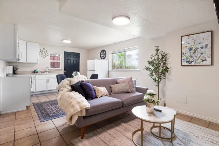 Open-concept living space featuring tiled flooring, a kitchen area with white cabinetry and a stainless steel sink, and a large window providing natural light