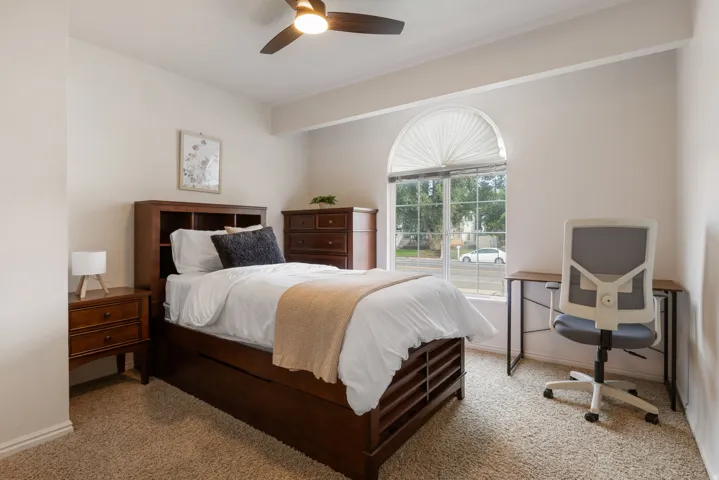 Arched window with pleated shade, ceiling fan with integrated lighting, and neutral carpeting