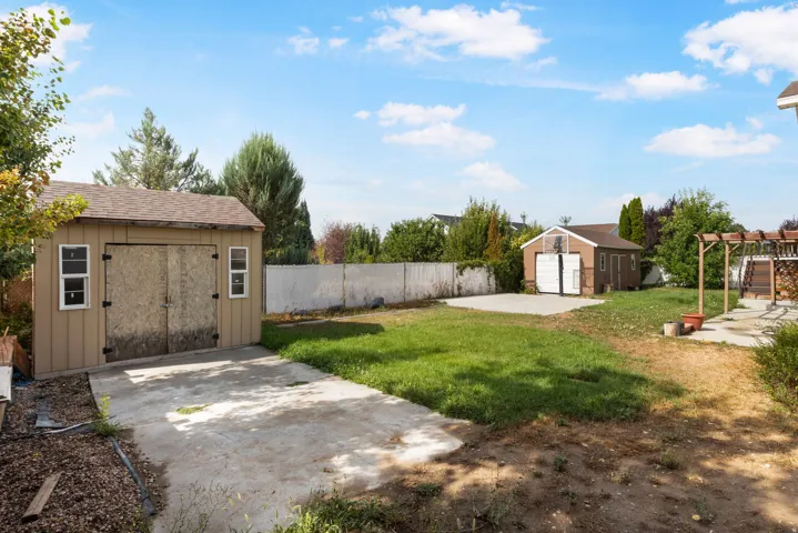 Expansive backyard featuring two detached sheds, a concrete patio area, and mature perimeter trees