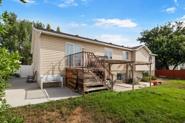 Exterior featuring tan siding, a multi-level wood deck with decorative metal railings, a sliding glass door, a concrete patio, and a wood pergola