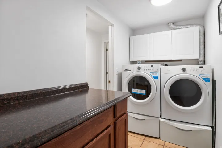 Built-in laundry appliances with pedestal bases, white upper cabinetry, and a dark stone-finish countertop over wood-finish cabinetry