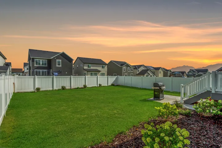 Expansive green lawn with perimeter fencing, a concrete patio, and a deck with stairs