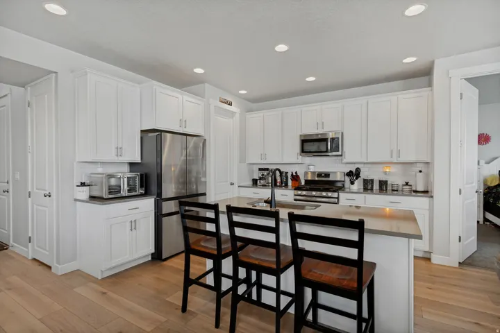 Kitchen featuring white shaker cabinetry, stainless steel appliances, a center island with bar seating, wood-finish flooring, and recessed lighting