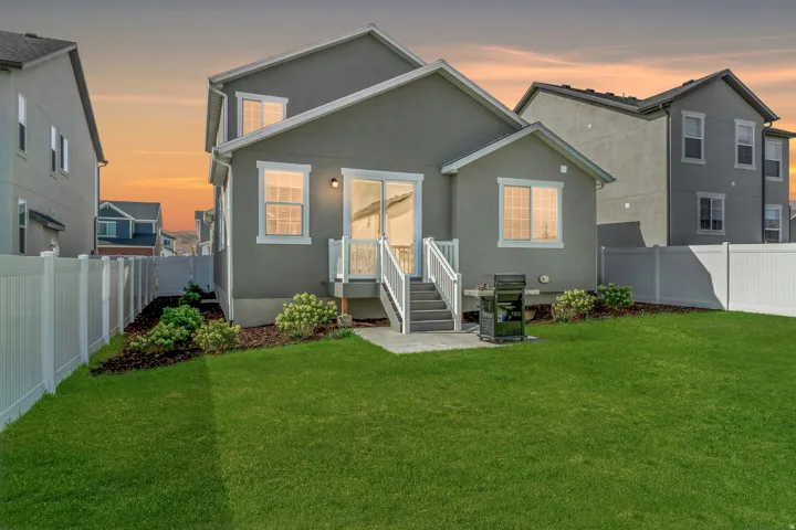 Expansive green lawn, white vinyl fencing, concrete patio, exterior lighting, and mature landscaping