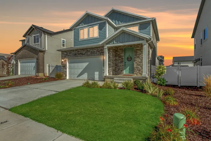 Two-story exterior with siding and stone accents, covered front porch, attached two-car garage, manicured lawn, and white privacy fence