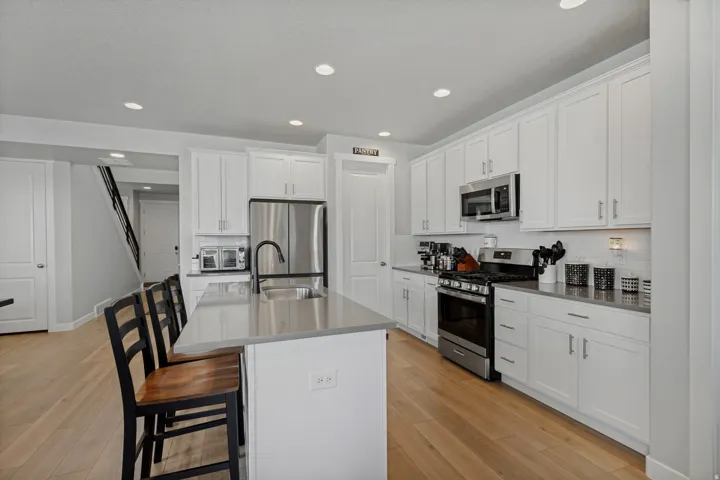 Kitchen featuring white shaker cabinetry, stainless steel appliances, a center island with sink, and wood-finish flooring